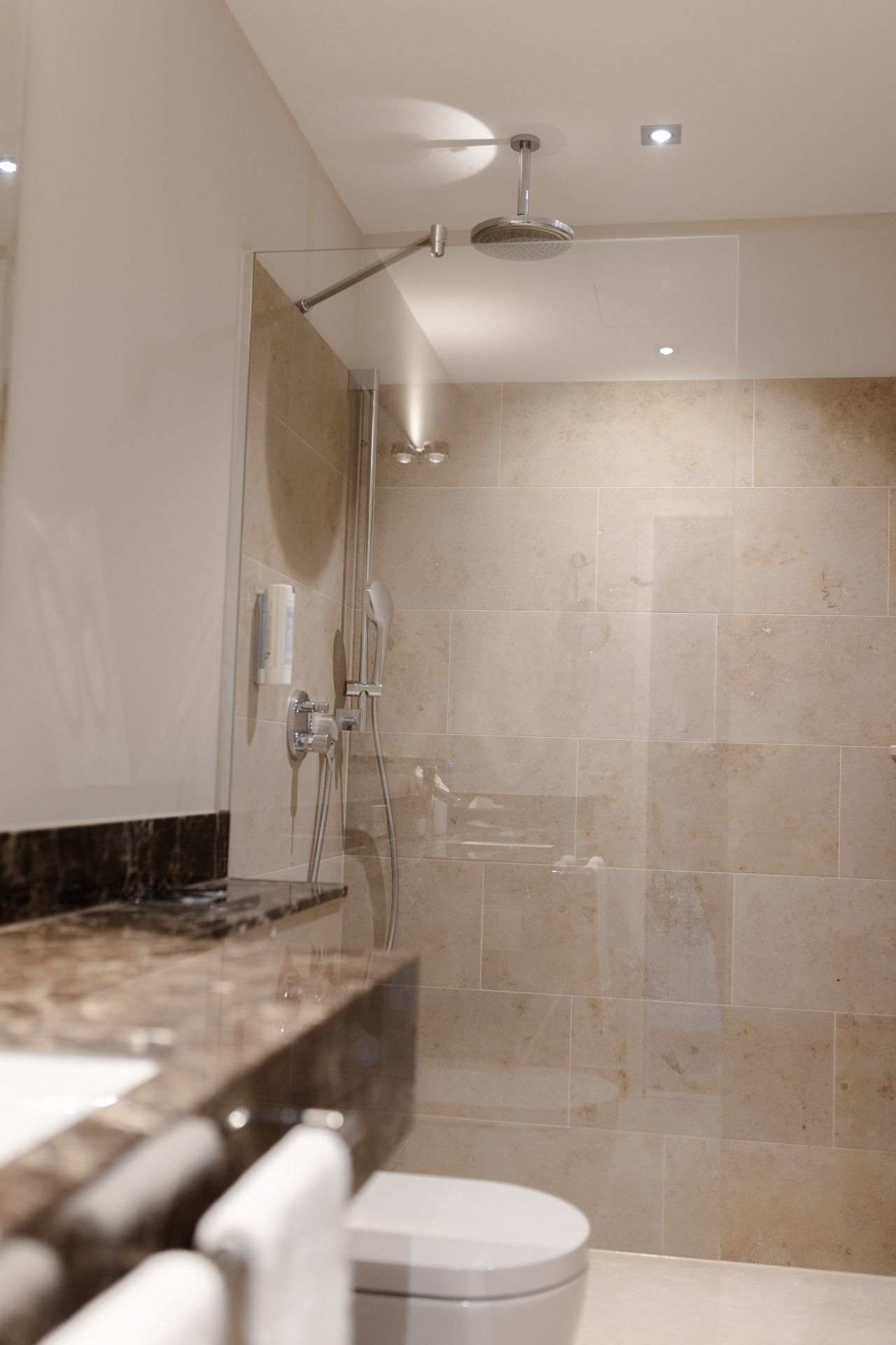 Luxuriöses Hotelbad nach Sanierung mit bodengleicher Dusche und Natursteinflächen